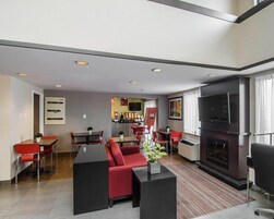 Una habitación de hotel moderna con televisor de pantalla plana, chimenea y zona de comedor con sillas rojas y una mesa.