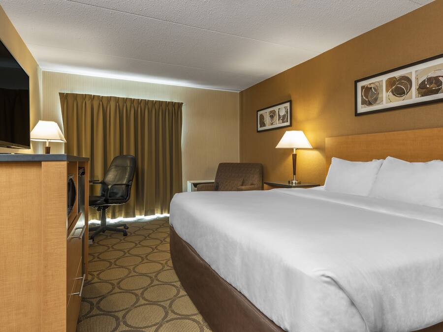 Une chambre d’hôtel avec un grand lit, un bureau avec une télévision, une chaise, une lampe de bureau et un tableau accroché au mur.