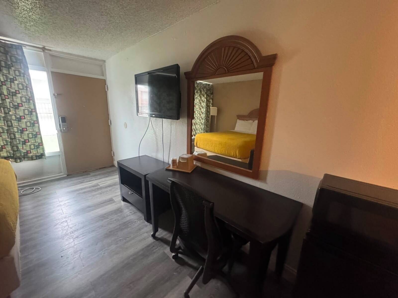 Una habitación de hotel con cama, escritorio, silla, televisión y espejo.
