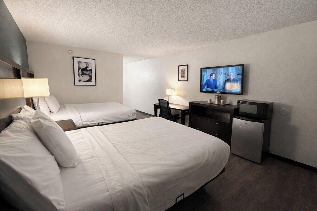 A hotel room with two beds, a desk, a television, and a refrigerator.