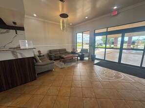 A reception area with a reception desk, seating, and large windows. - Express Inn & Suites Greensville TX (Greenville)