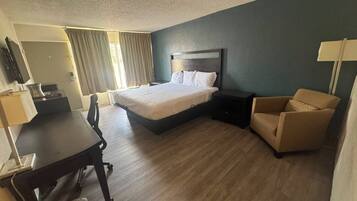 A hotel room with a bed, a desk, a chair, and a lamp.