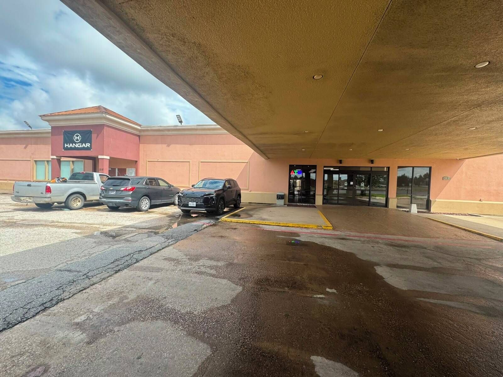 A parking lot with vehicles, a building entrance, and a covered area.