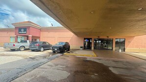 Un parking avec des véhicules, l’entrée d’un bâtiment et une zone abritée.