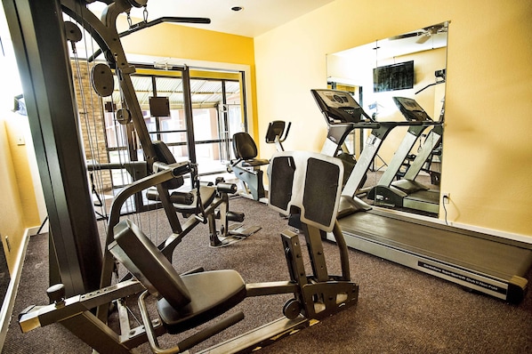 A gym with cardio machines, weight training equipment, and a mirrored wall.