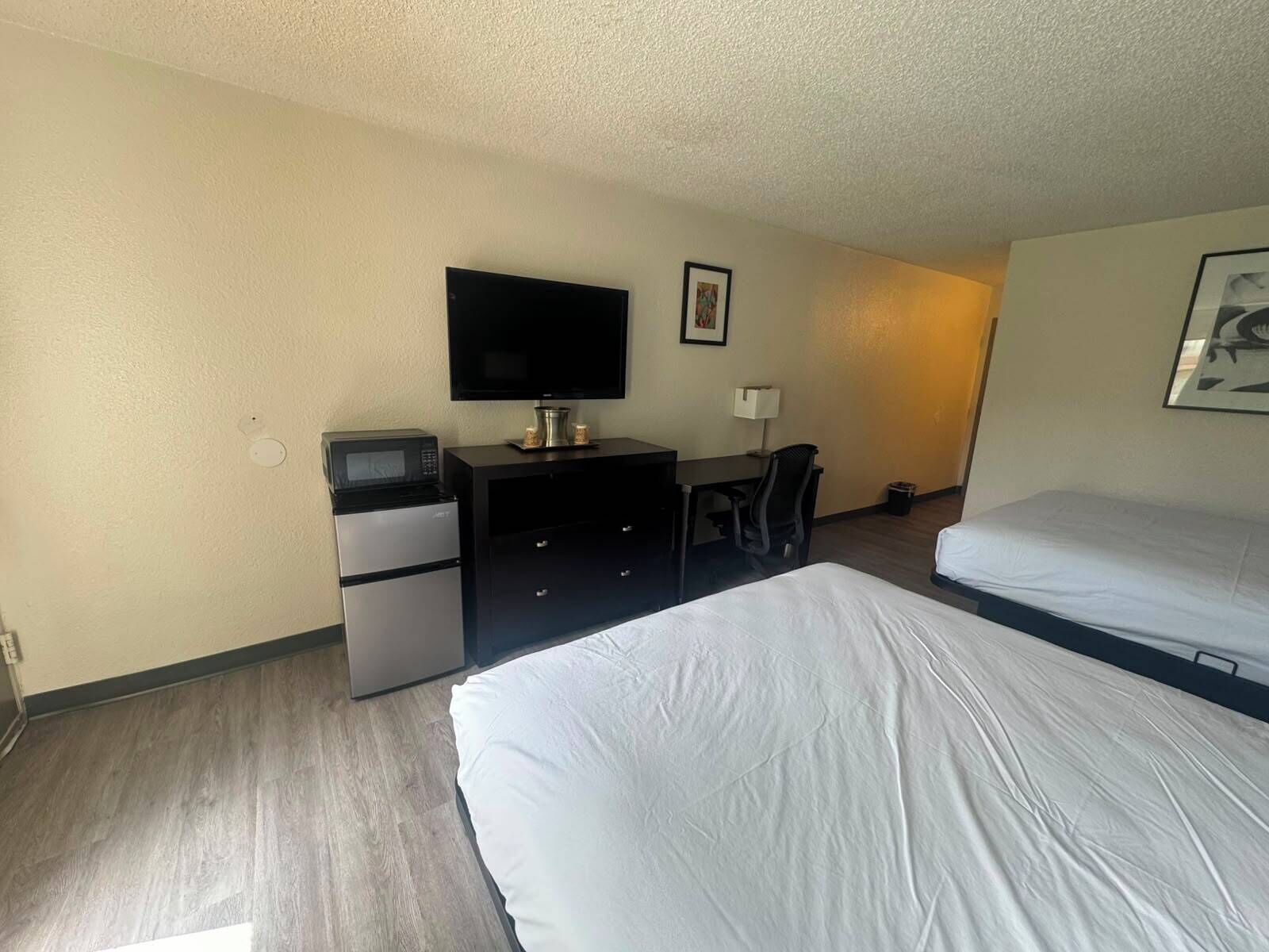 A hotel room with a bed, a desk with a computer, a television, and a minibar.