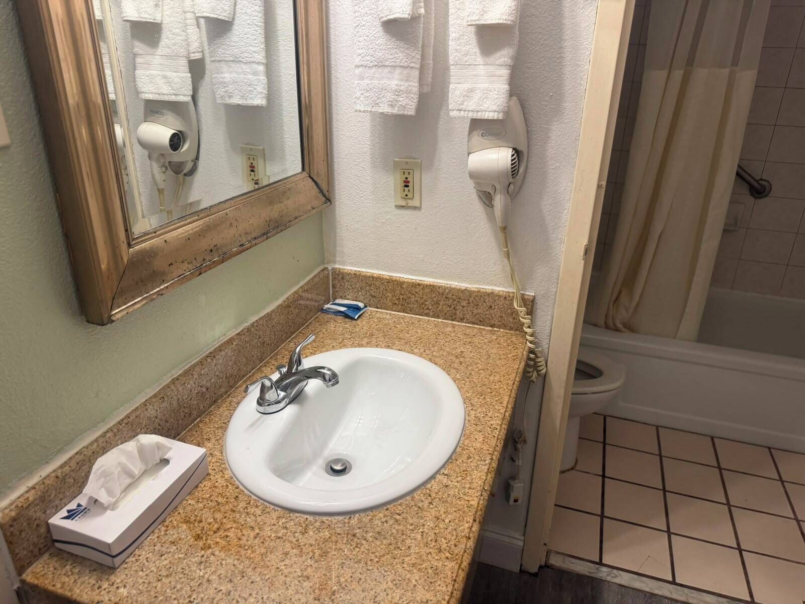 A bathroom with a sink, mirror, towel rack, and a shower area.