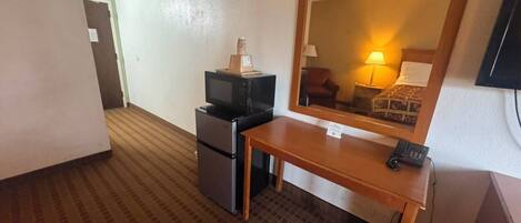 A hotel room with a kitchenette, a wooden desk, a telephone, and a large mirror.