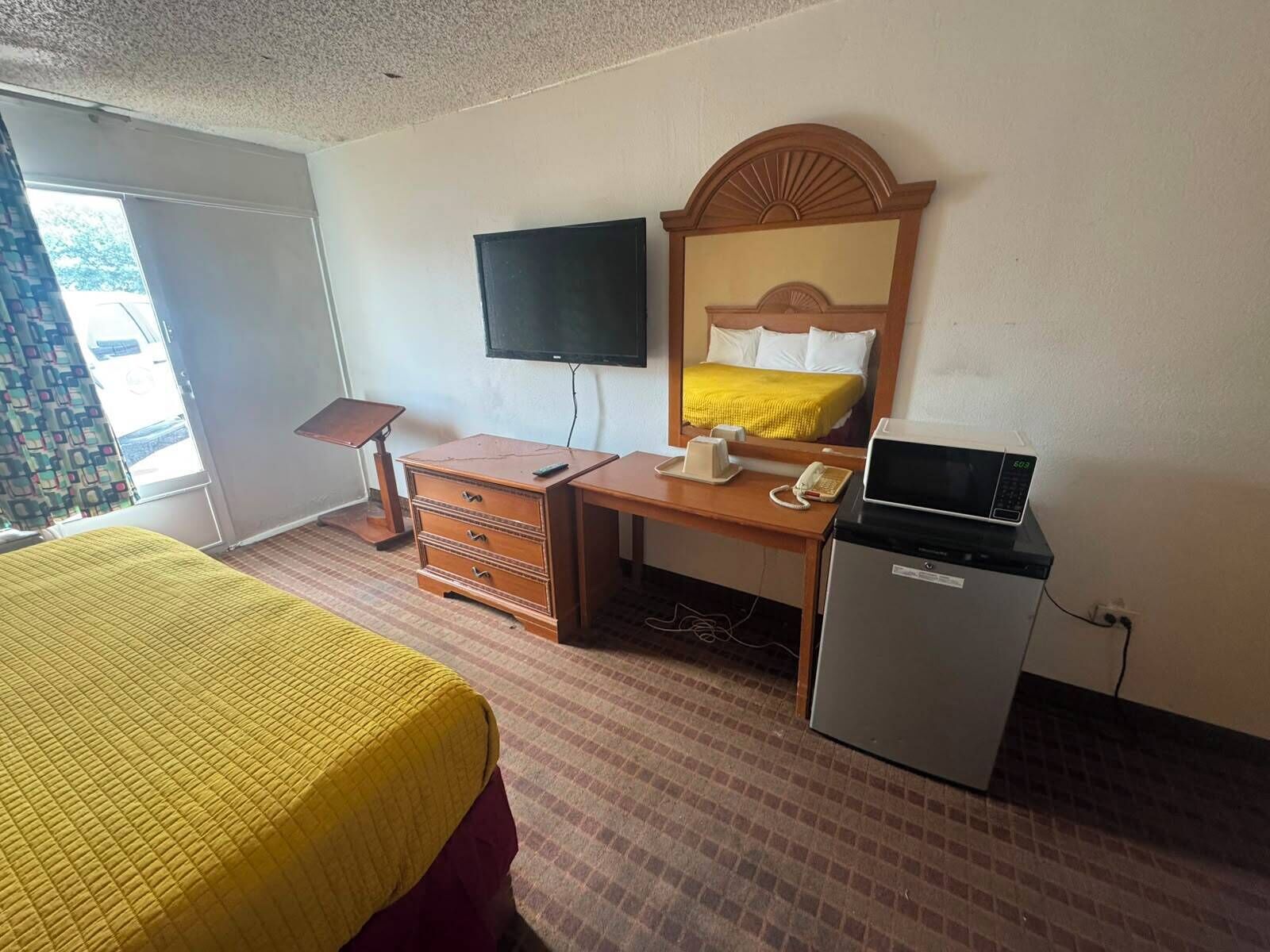 Habitación de hotel con cama, escritorio, teléfono, microondas, televisión y refrigerador pequeño.