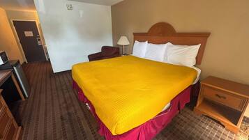 A hotel room with a large bed, a wooden headboard, a desk with a lamp, and a small wooden nightstand.