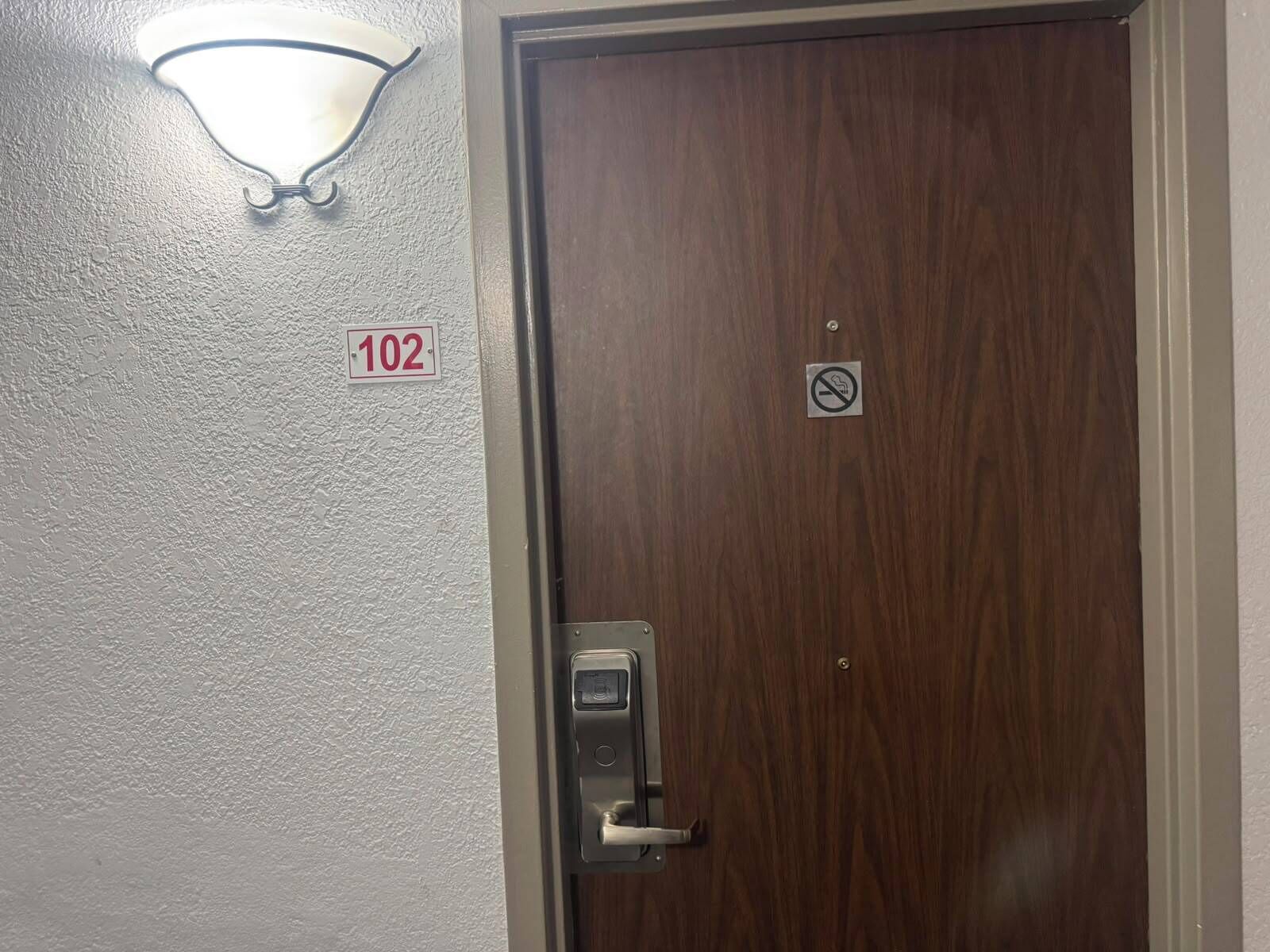 Puerta con un letrero de no fumar, cerradura con teclado numérico e indicación de la habitación 102.