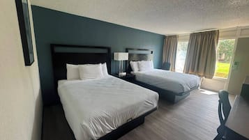 A hotel room with two beds, a desk, and a window with curtains.