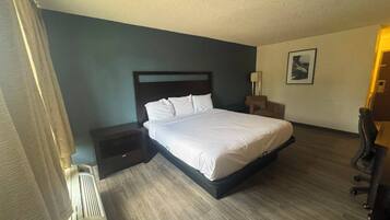 Una habitación de hotel con cama, mesitas de noche, una silla, un escritorio y una lámpara.