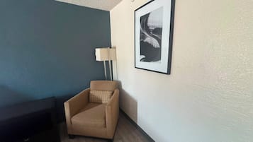 A room with a beige armchair, a framed picture on the wall, and a floor lamp.