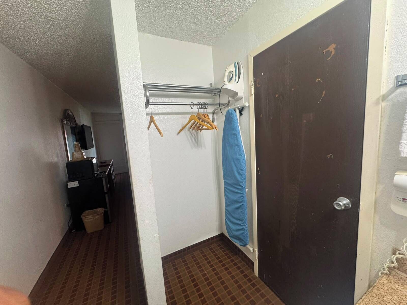 A narrow hallway with a tiled floor, a black door, a blue shower curtain, and a clothes drying rack with hangers.