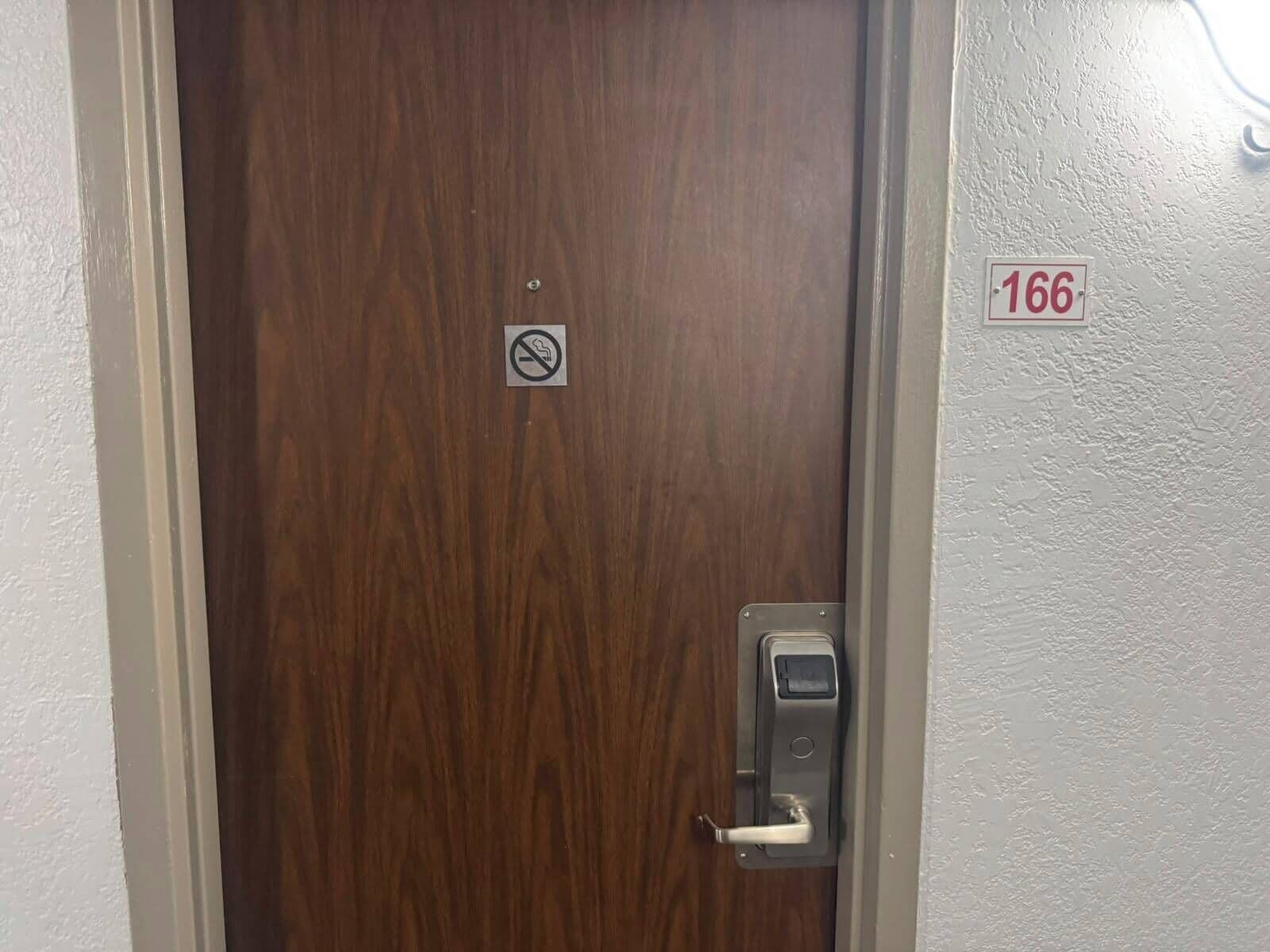Een houten deur met een rookvrij bord, een deurbel en een bord met het kamer nummer 166.
