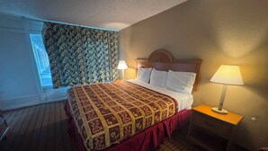 Une chambre d’hôtel avec un grand lit, deux lampes de chevet, une fenêtre avec des rideaux à motifs et une tête de lit en bois.
