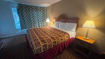 A hotel room with a large bed, two bedside lamps, a window with patterned curtains, and a wooden headboard.