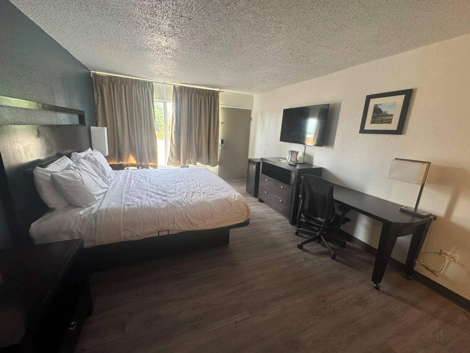Une chambre d’hôtel équipée d’un lit, d’un bureau, d’une chaise, d’une télévision et d’une fenêtre avec des rideaux.