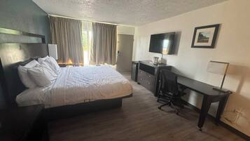 Une chambre d’hôtel équipée d’un lit, d’un bureau, d’une chaise, d’une télévision et d’une fenêtre avec des rideaux.