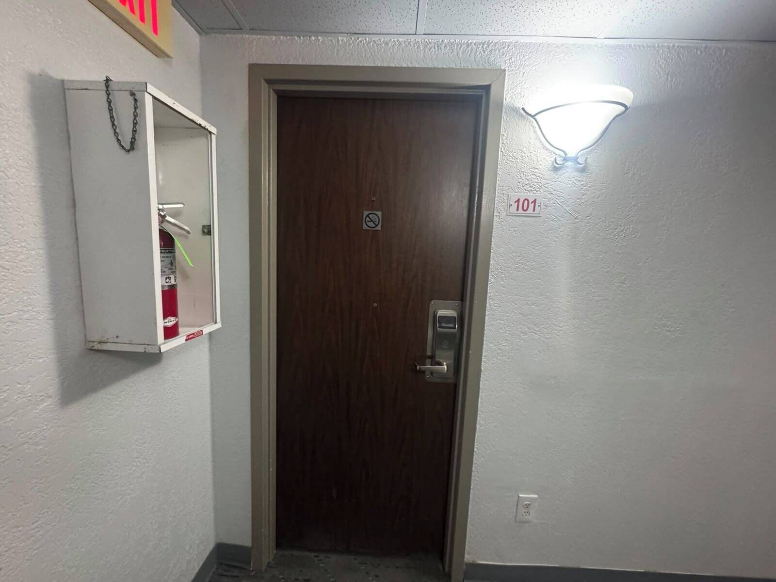 A door with a digital lock, a fire extinguisher, and a wall-mounted light fixture.