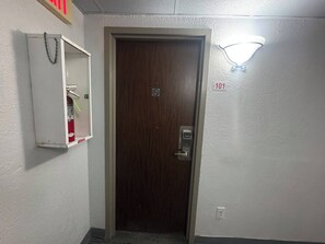 A door with a digital lock, a fire extinguisher, and a wall-mounted light fixture. - Express Inn & Suites Greensville TX (Greenville)