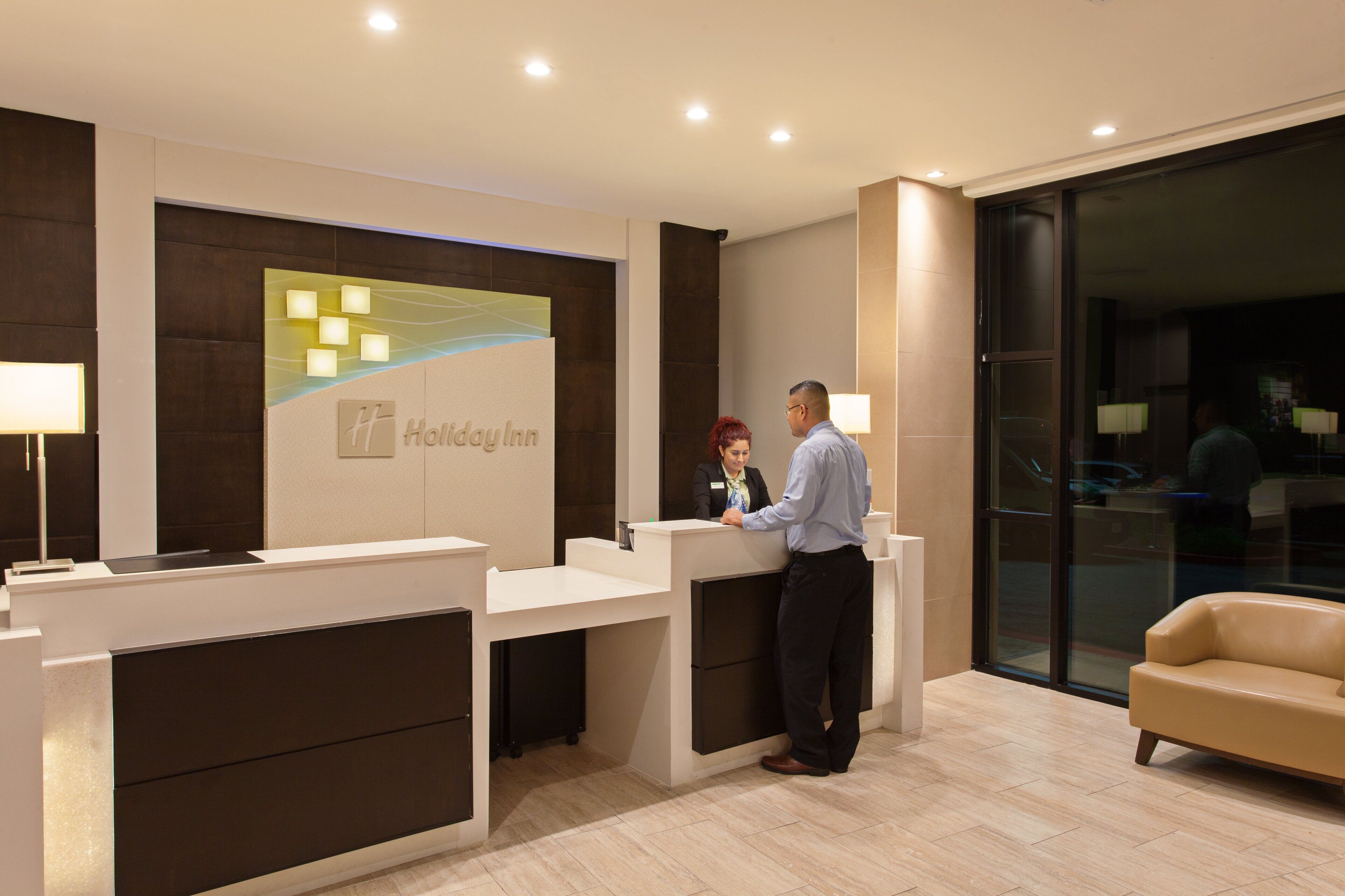 A reception desk with a Holiday Inn sign, a sofa, and a glass door leading to a dark interior.