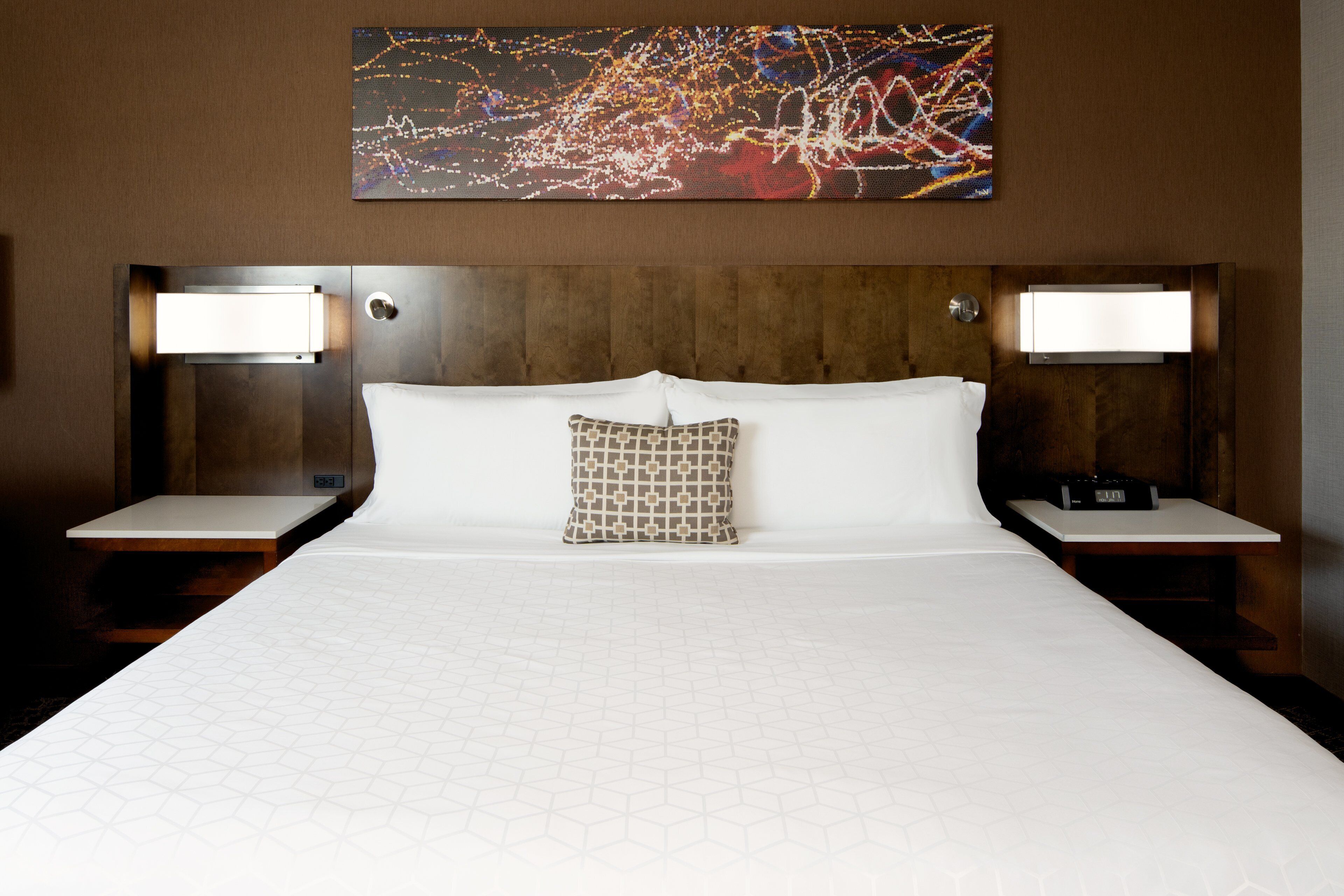 Habitación de hotel con una cama grande, dos mesitas de noche, un cabecero y un cuadro abstracto colgado en la pared.