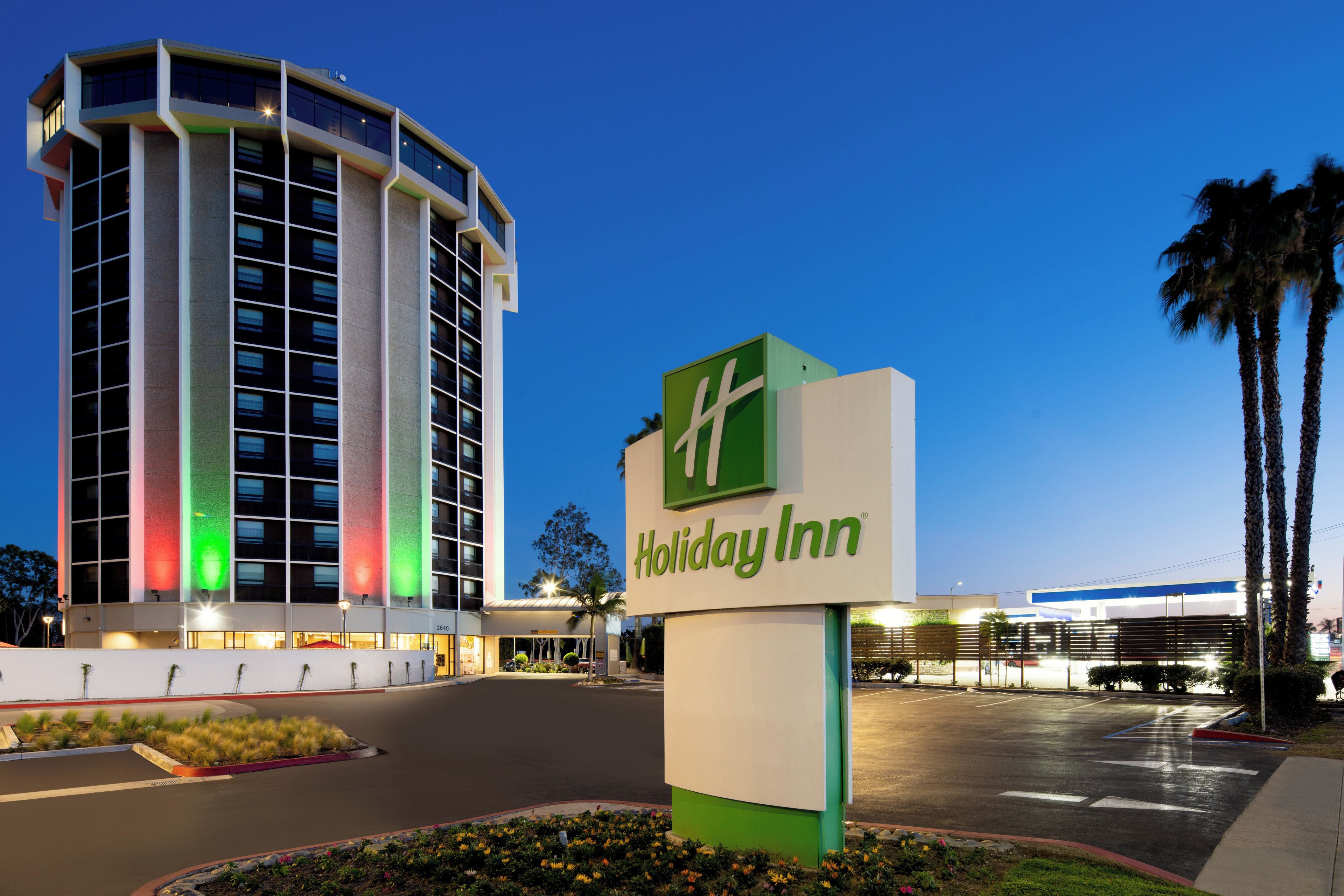 Un hotel Holiday Inn con un letrero llamativo, un estacionamiento y un edificio grande con varios pisos al fondo.