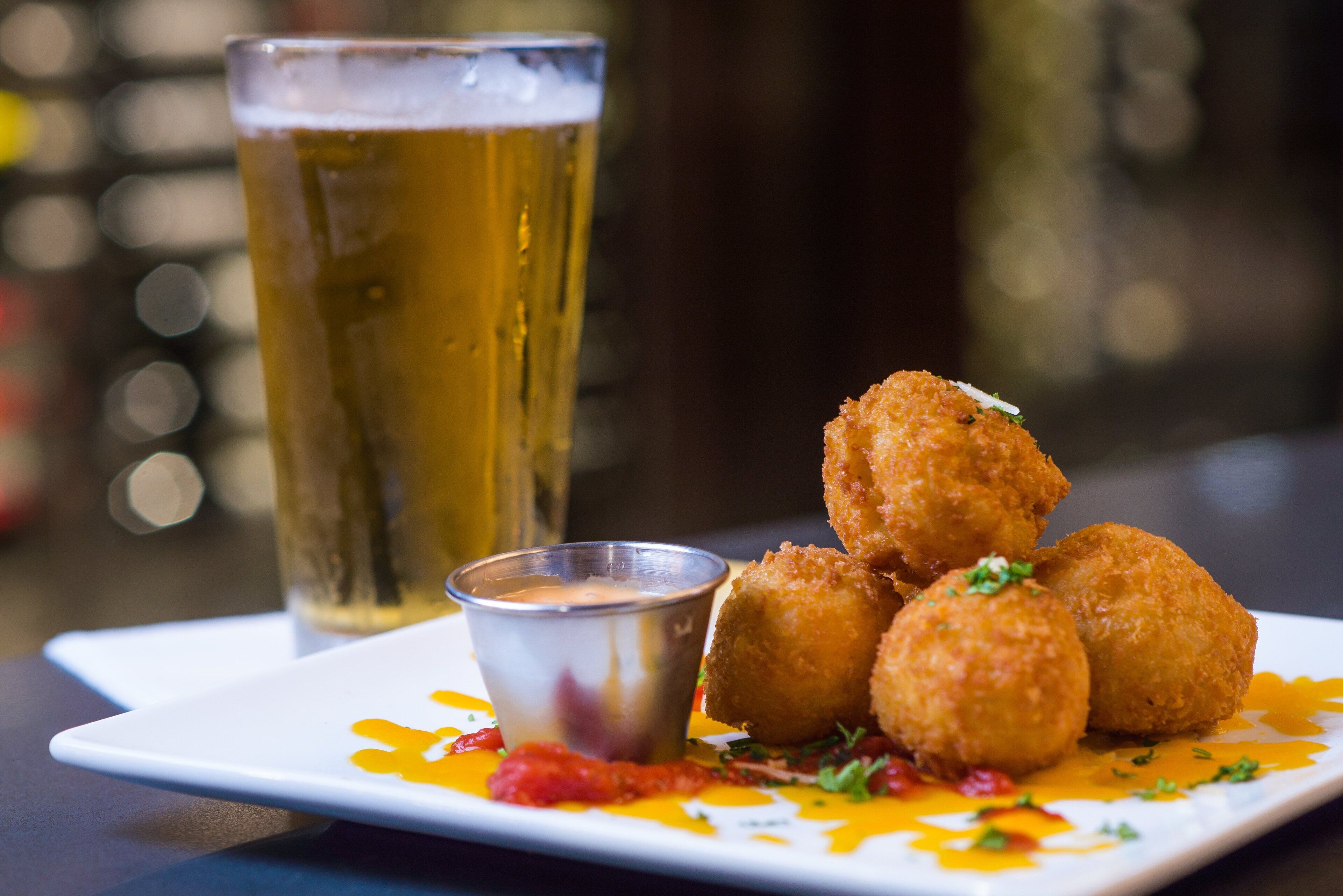Une assiette de boulettes frites, accompagnées d’une sauce pour tremper, et un verre de bière.