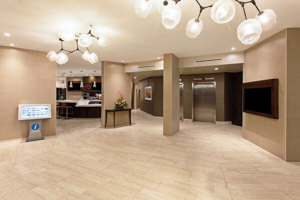 A spacious lobby with a reception desk, a digital information kiosk, and a modern elevator.