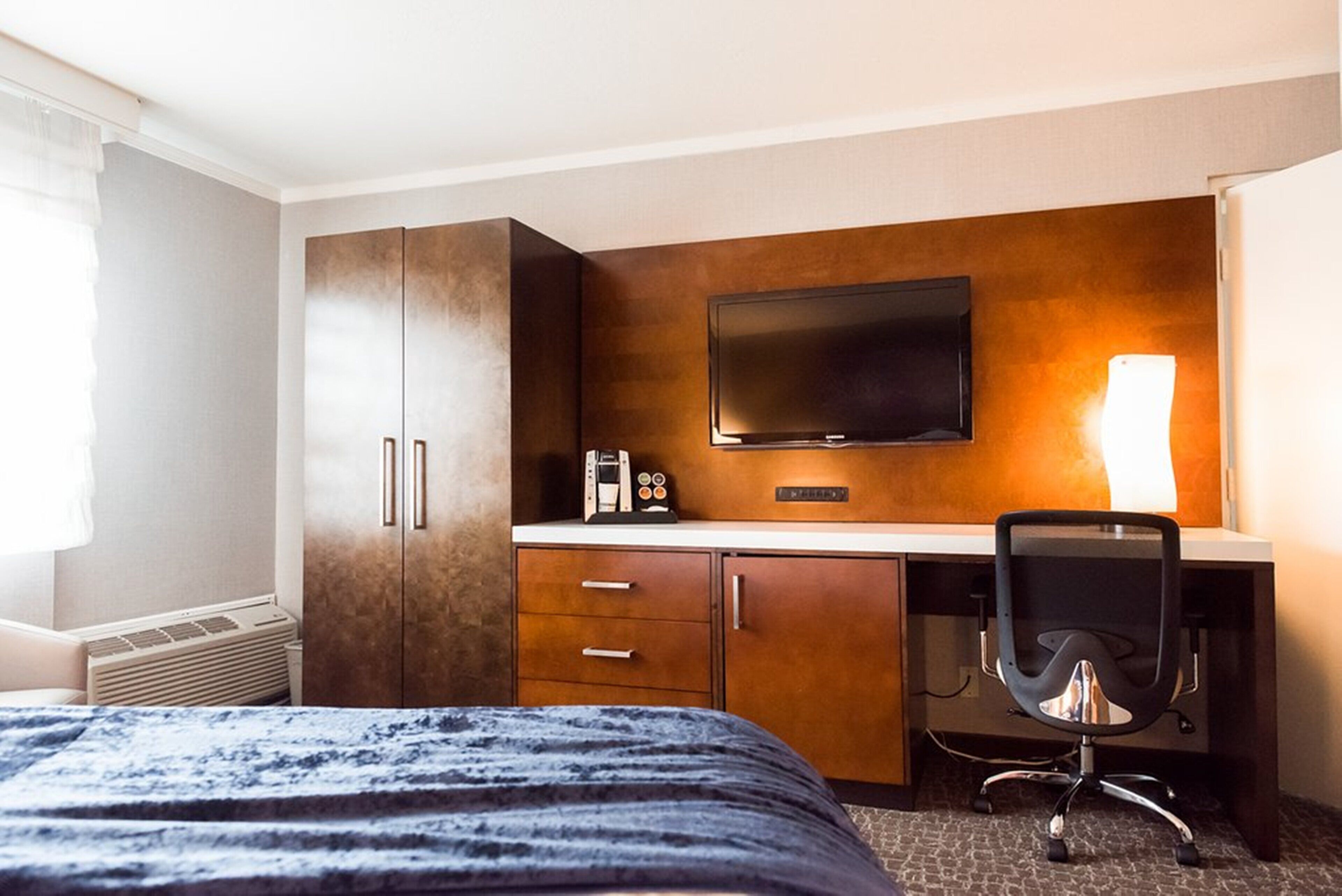 A hotel room with a bed, a desk with a chair, a TV, and a coffee maker.