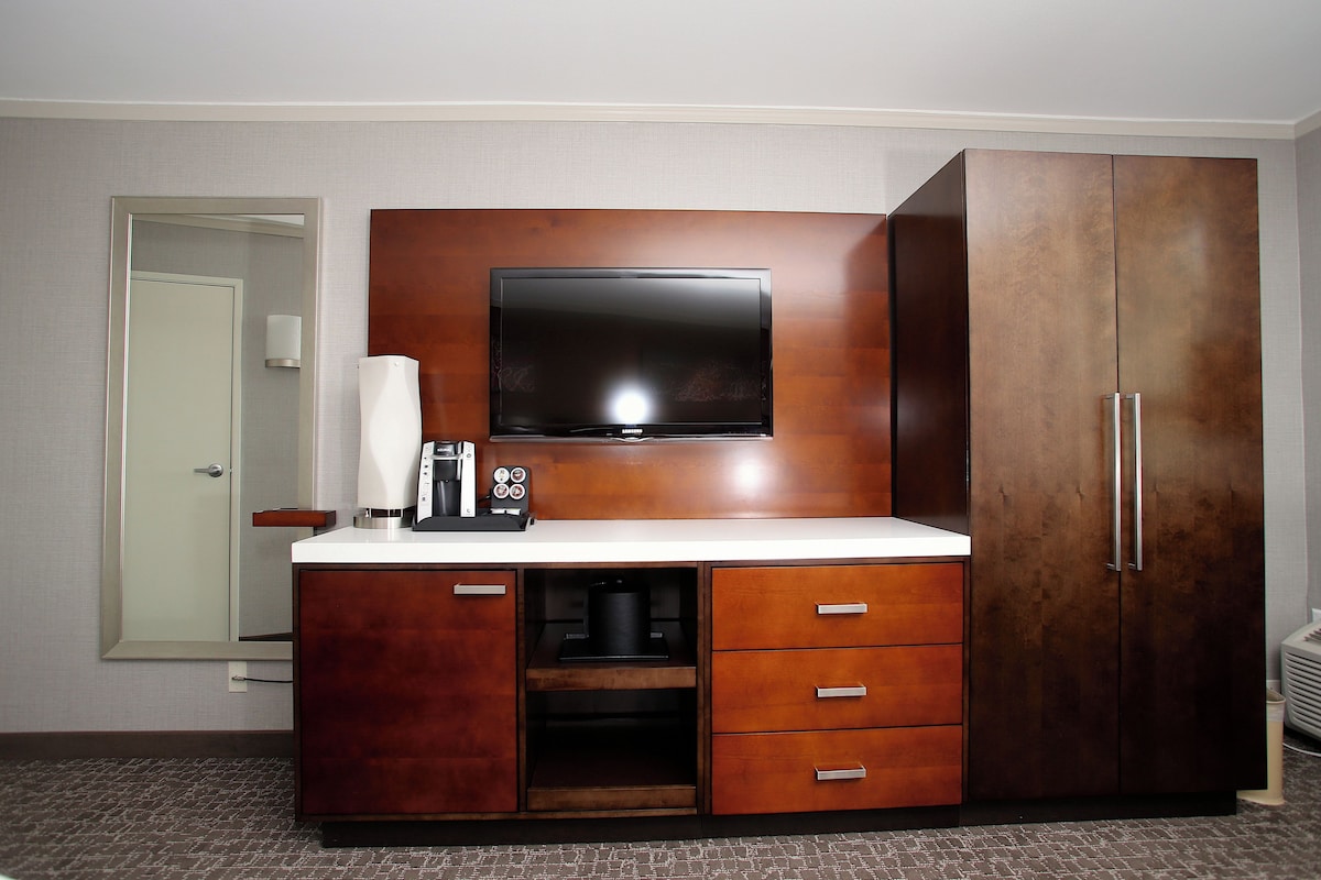A hotel room with a wooden cabinet, a flat-screen TV, a coffee maker, and a minibar.