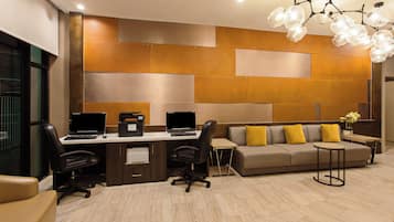 Un espace de bureau moderne comprenant un bureau, deux ordinateurs portables, une imprimante, un canapé avec des coussins jaunes et un luminaire au plafond au design original.