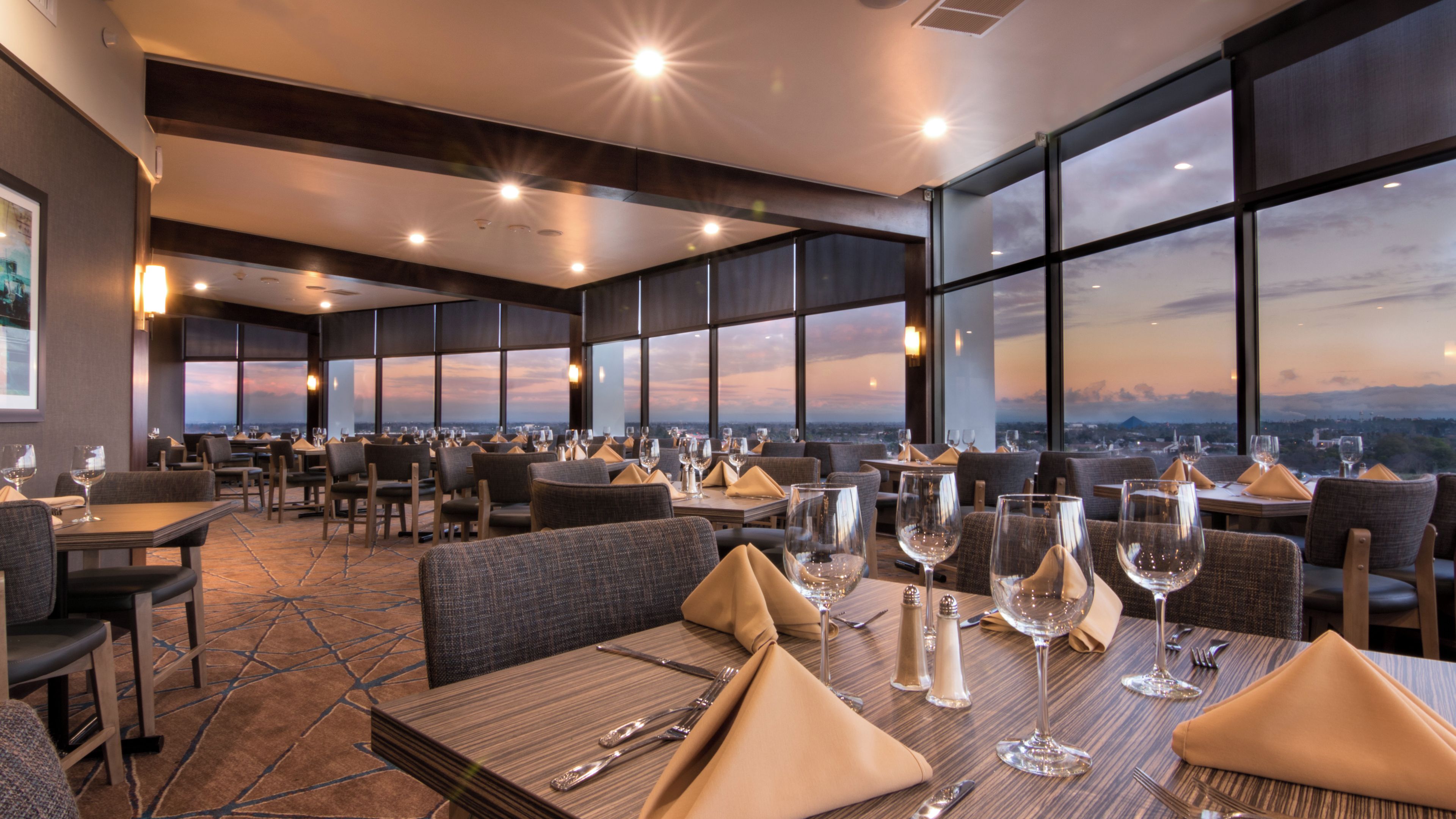 A restaurant with tables set for dining, large windows offering a view, and a modern interior design.