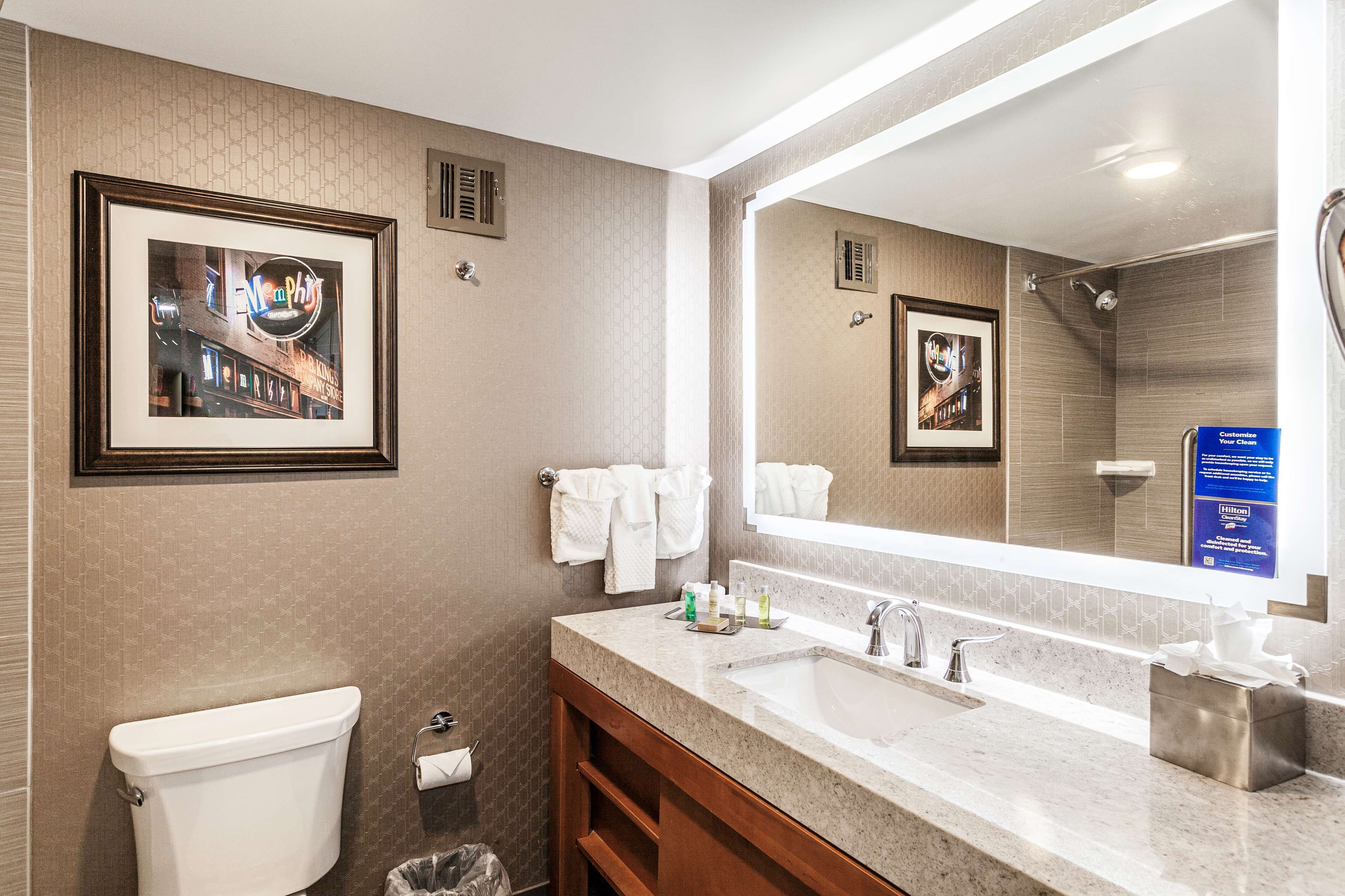A hotel bathroom with a toilet, sink, mirror, and framed pictures on the wall.