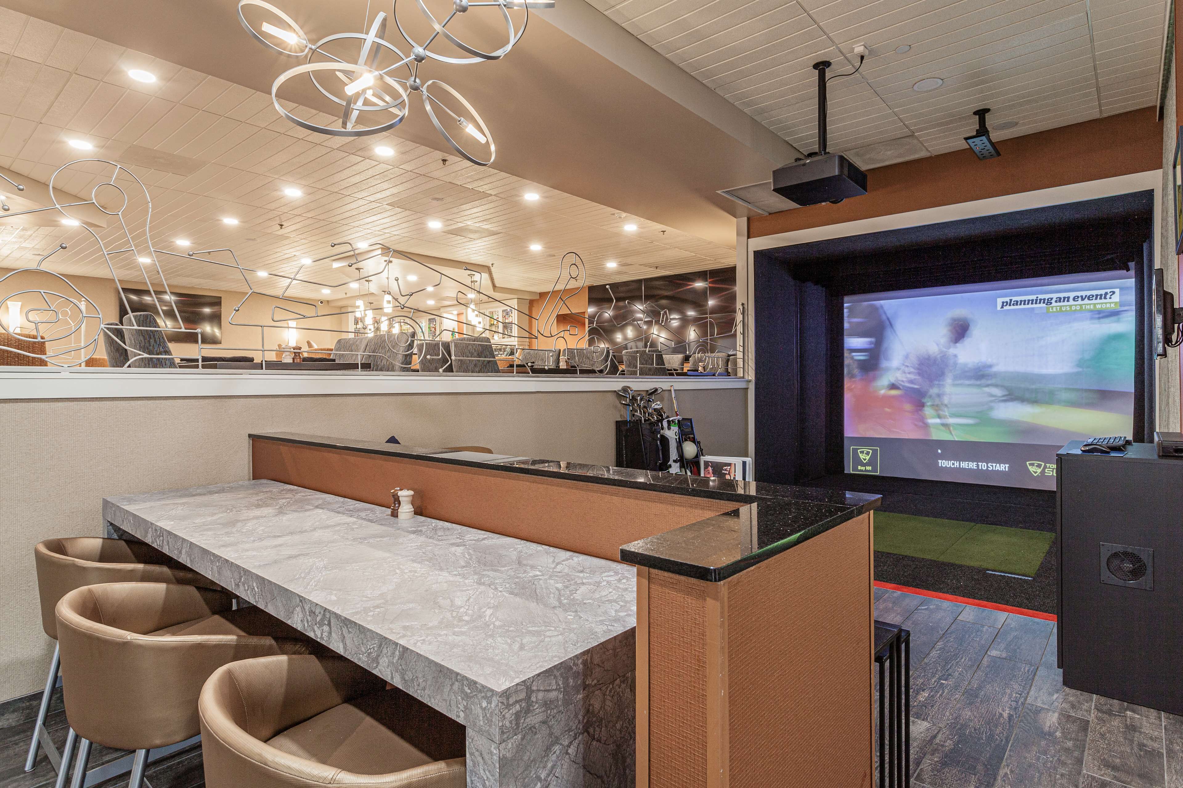 A modern bar area with a marble countertop, cushioned bar stools, and a large screen displaying a sports event.