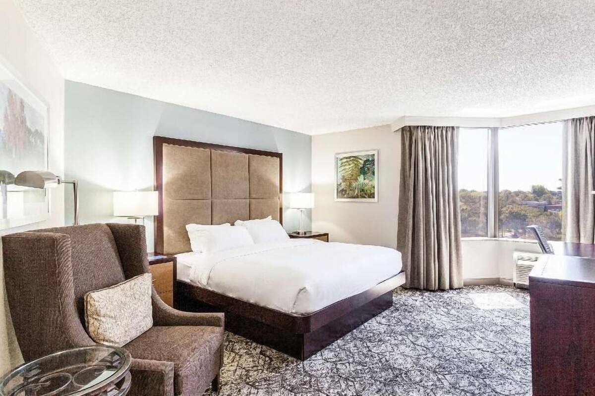 A hotel room with a large bed, a chair, a desk, and a view of the outdoors.