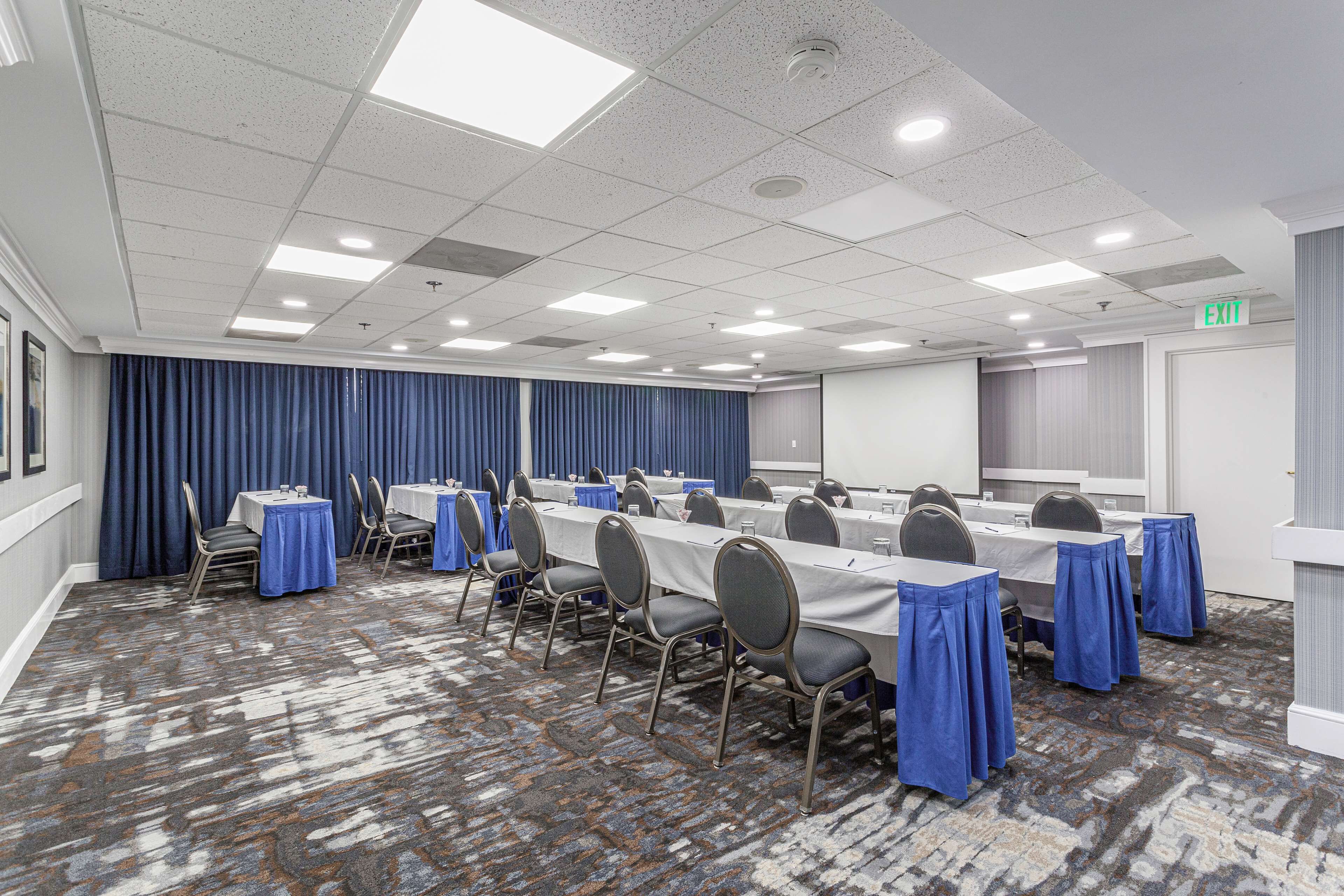 Une salle de conférence équipée de tables et de chaises, dotée d’un sol recouvert de moquette et d’un plafond avec des luminaires.
