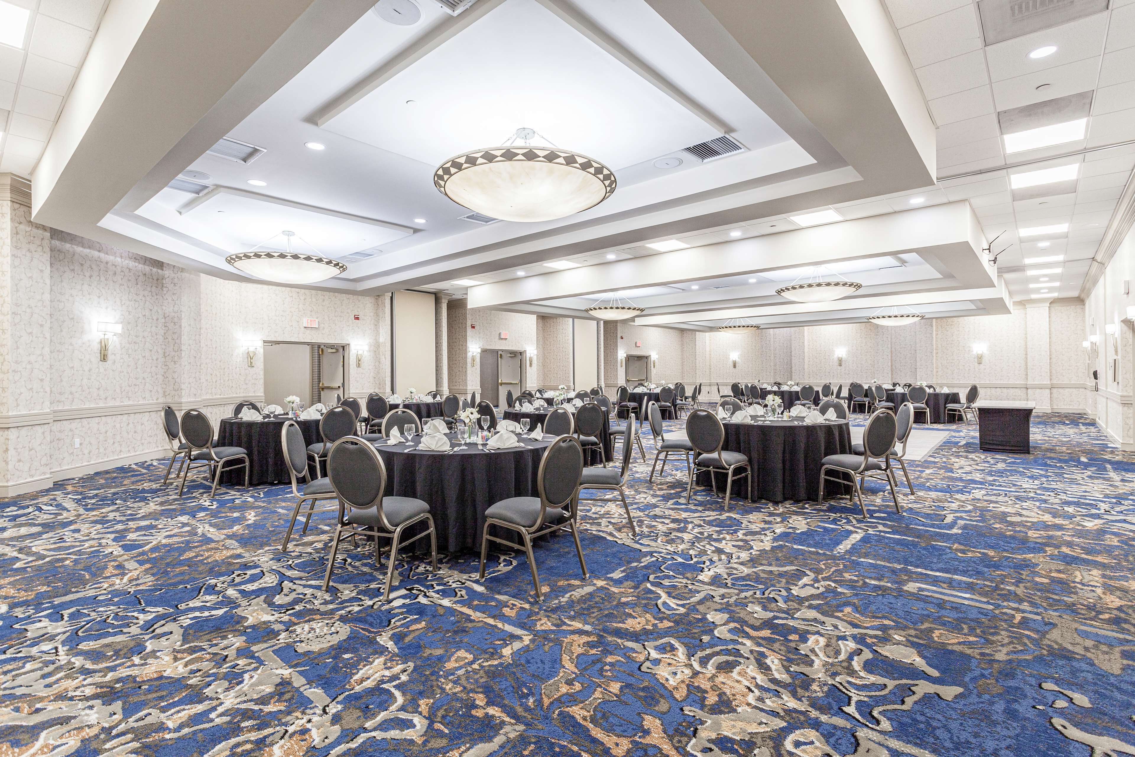 A large conference room with round tables and chairs, a patterned carpet, and a high ceiling with recessed lighting.