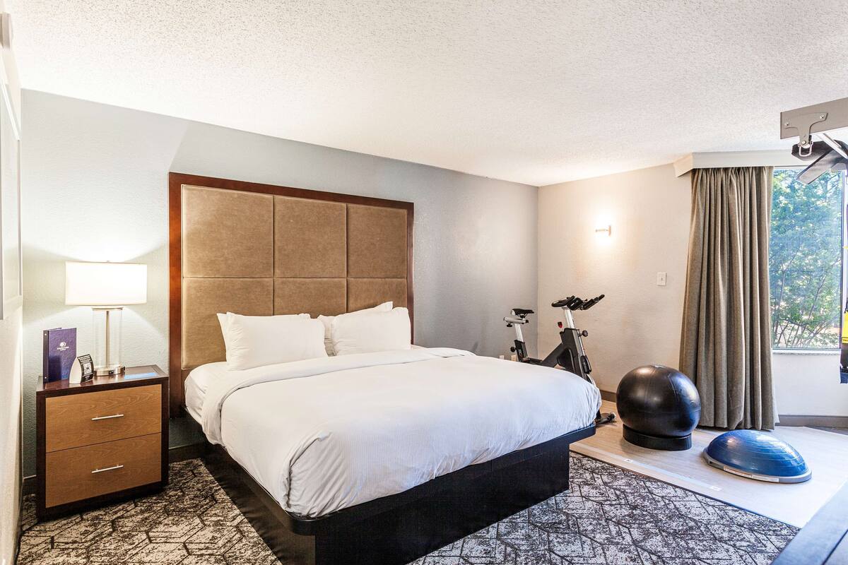 A hotel room with a large bed, a nightstand with drawers, a lamp, a massage ball, and a yoga mat.