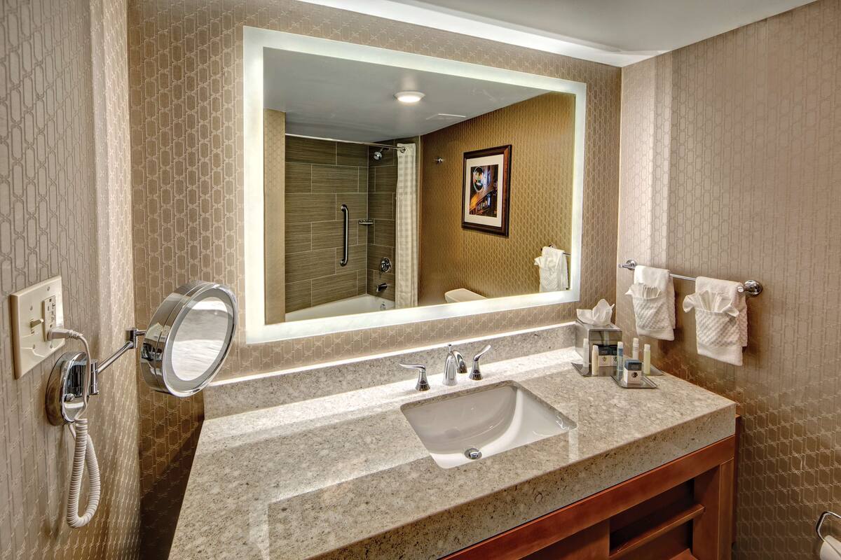 A bathroom with a large mirror, a sink, and a shower.