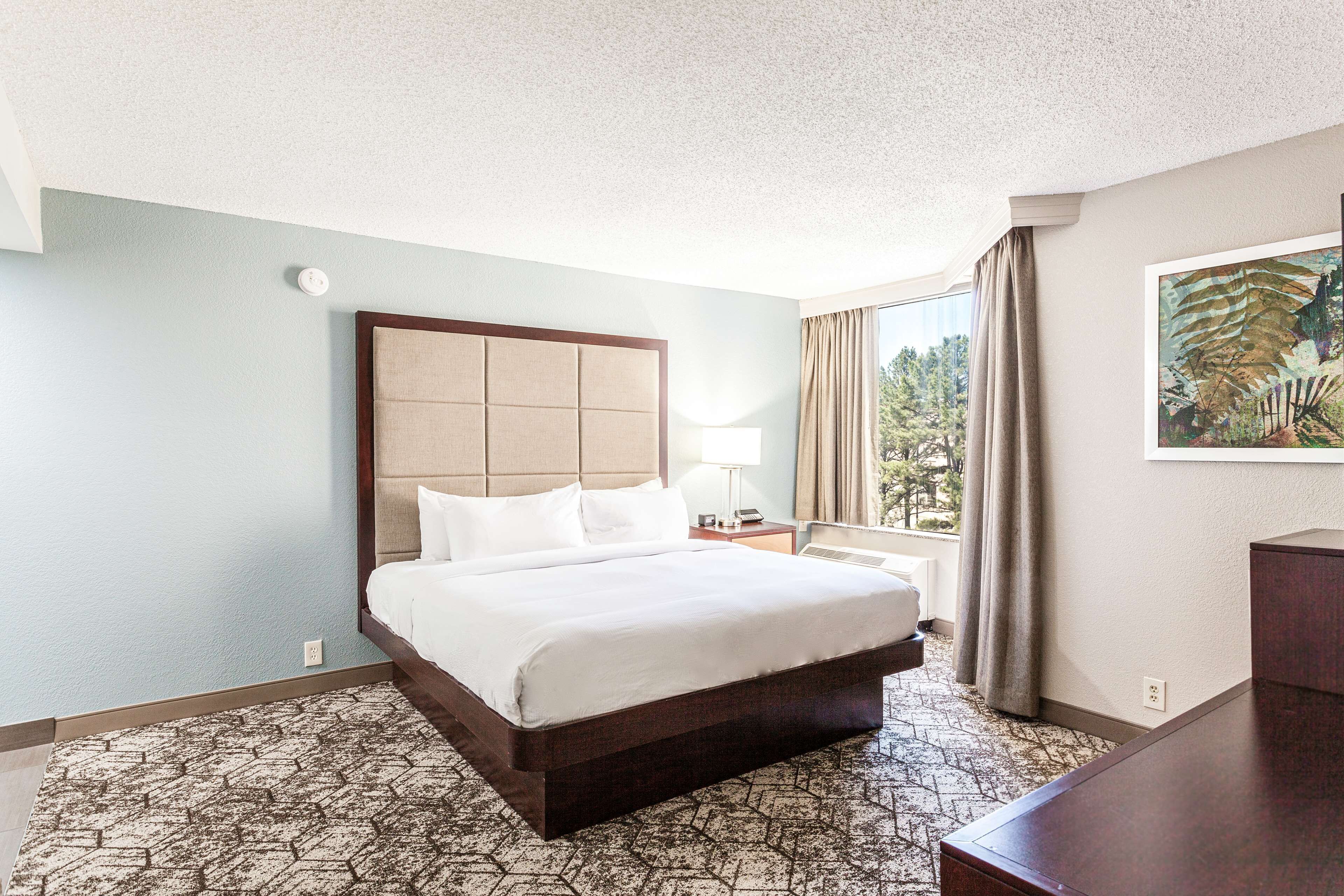 A hotel room with a large bed, a nightstand, a lamp, and a painting on the wall.