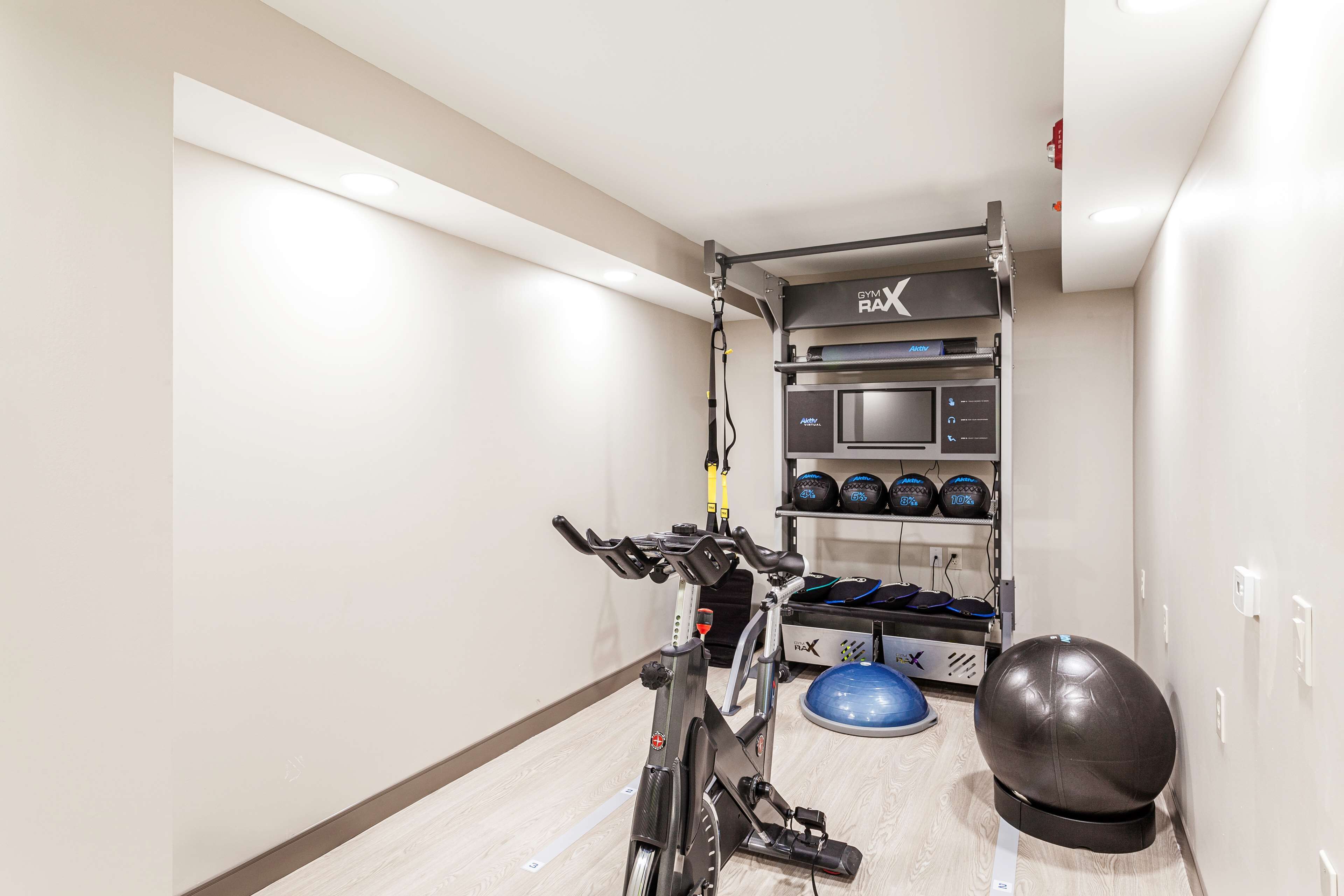Un gimnàs amb una bicicleta estatica, una pilota blava d'exercici i un suport amb equipament esportiu.