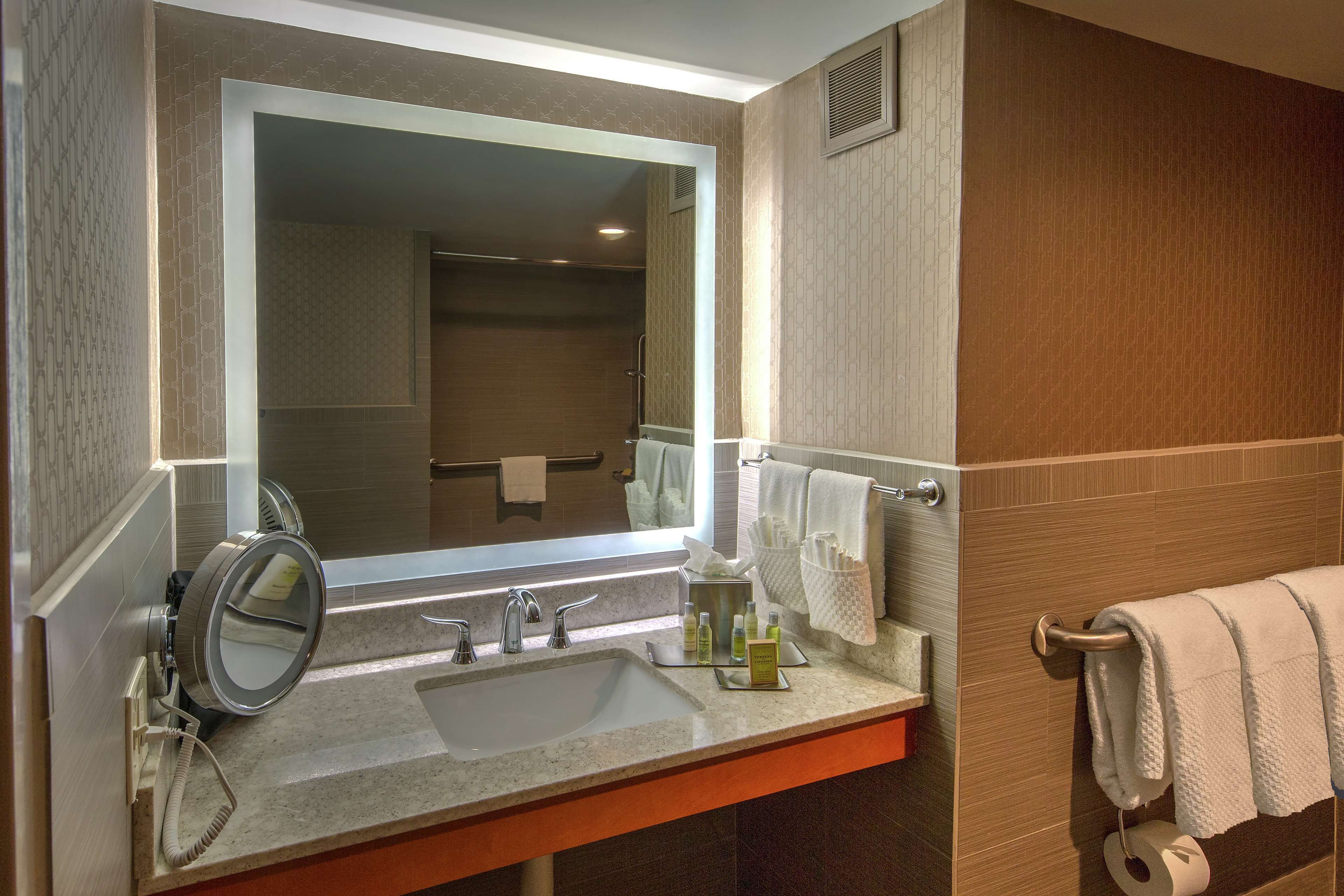 A bathroom with a large mirror, a sink, and a towel rack.
