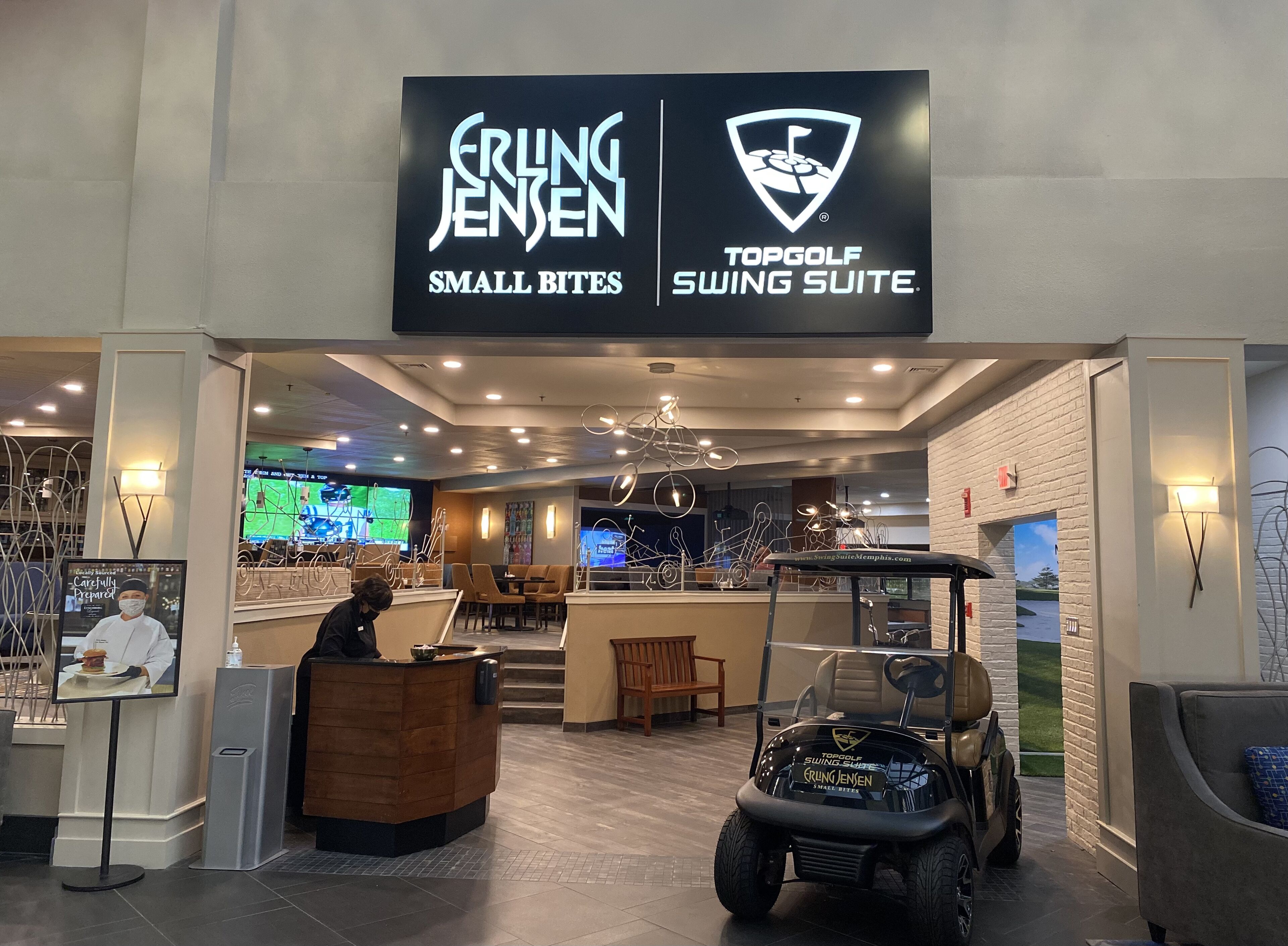 A golf-themed restaurant interior with a reception desk, seating area, and a golf cart.