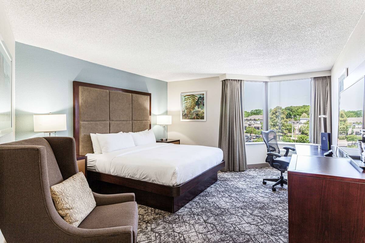 A hotel room with a large bed, a desk, a chair, and a view of the city.