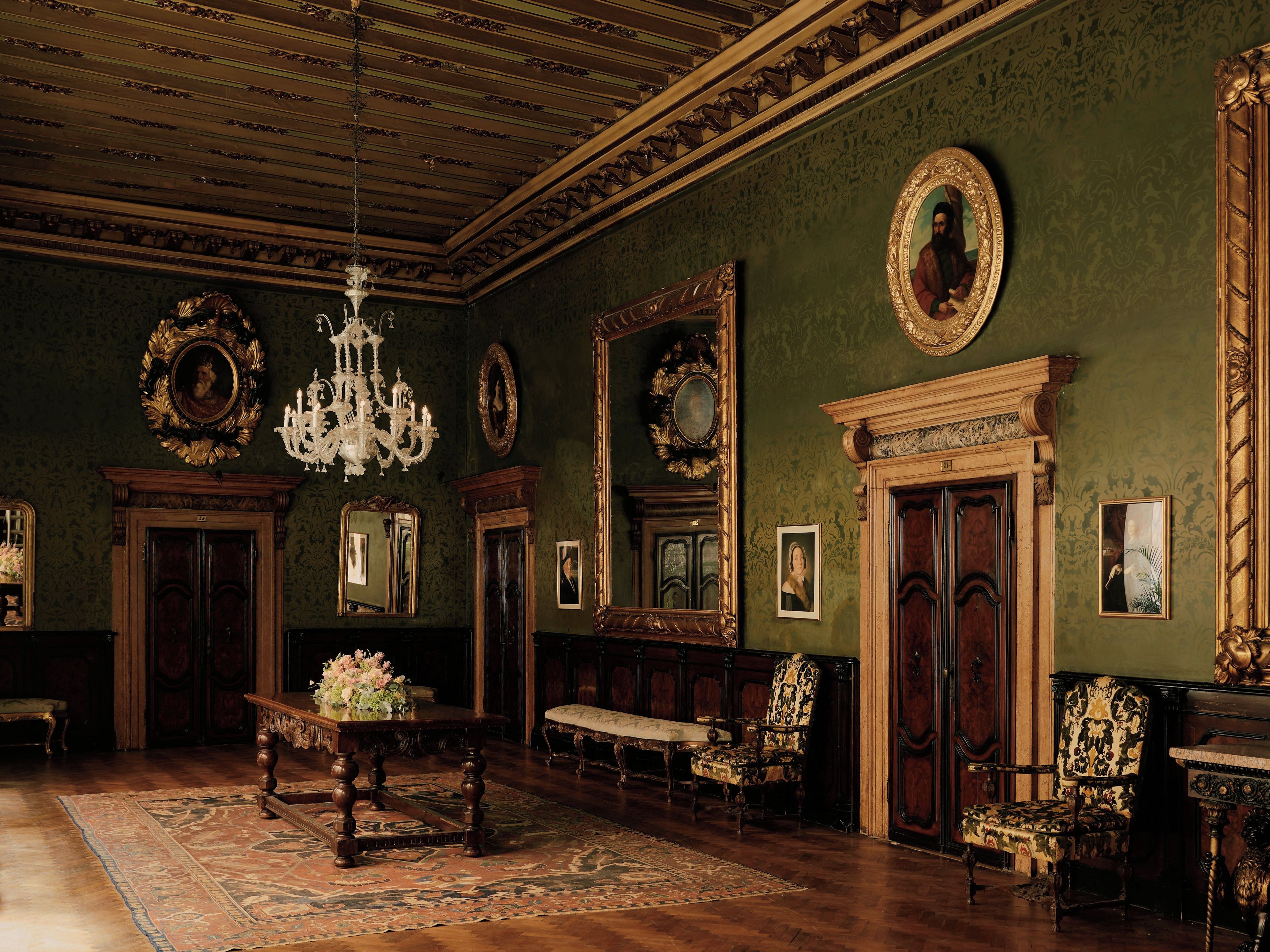 A grand room with ornate woodwork, a chandelier, and multiple framed portraits on the walls.