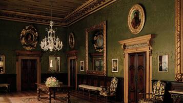 A grand room with ornate woodwork, a chandelier, and multiple framed portraits on the walls.
