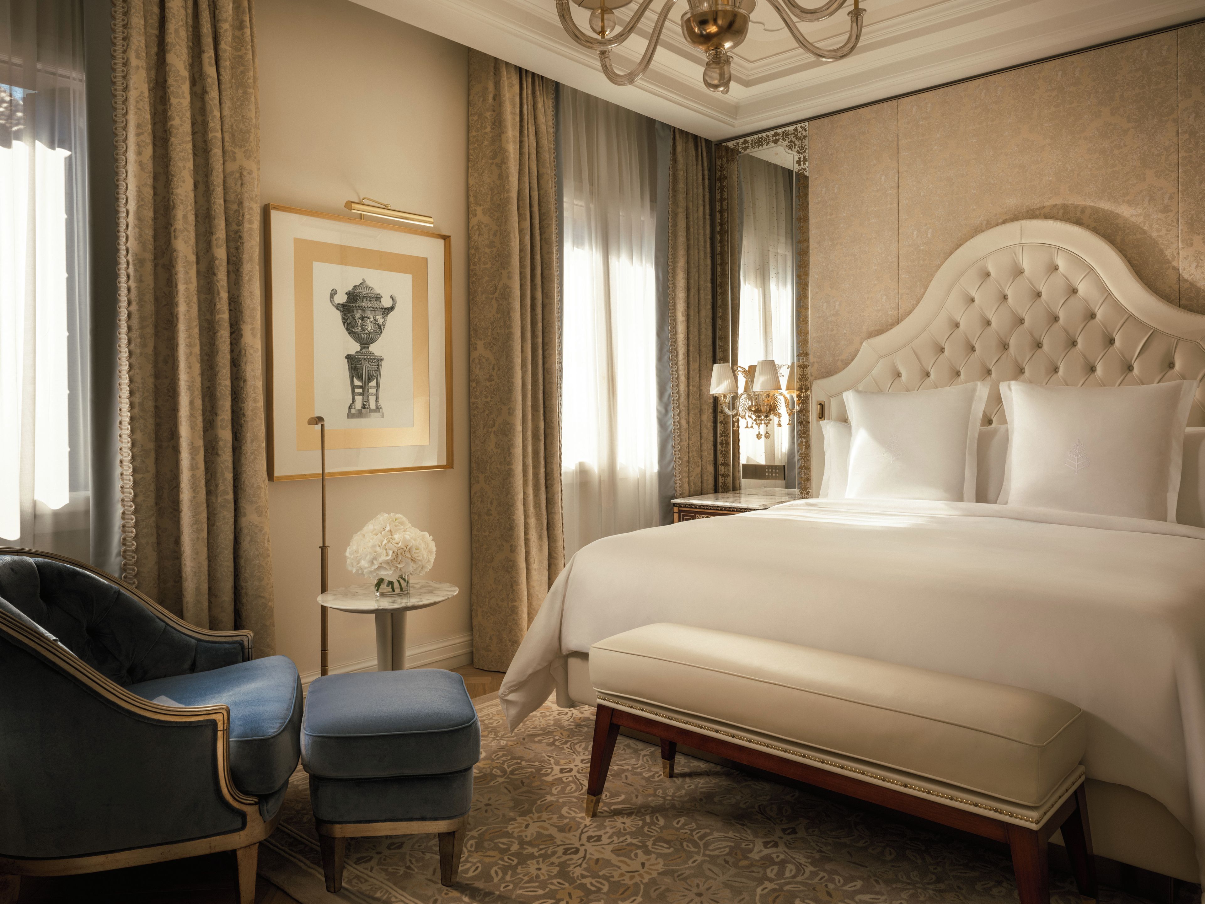 Una camera d'albergo con un letto grande, una sedia, un tavolino con un vaso e un quadro appeso al muro.